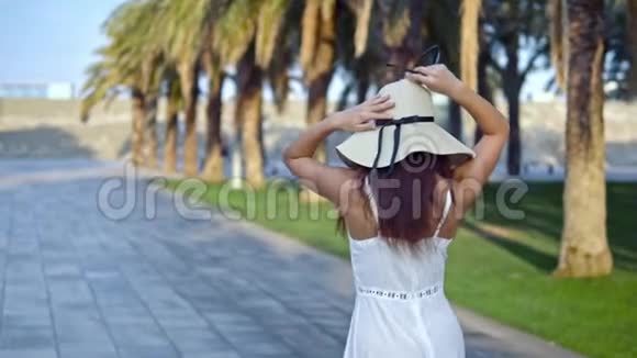 穿着白色裙子戴着帕梅拉帽子走路的漂亮女人视频的预览图