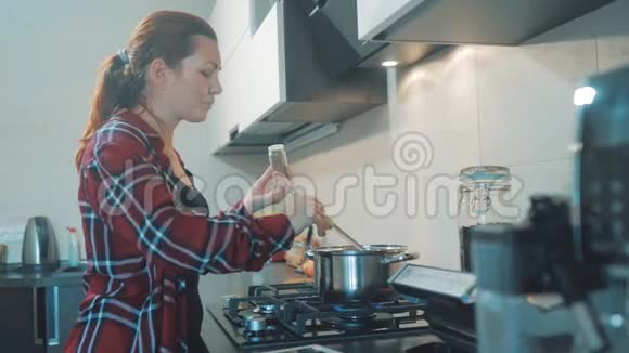 女人在厨房里煮汤锅防止锅里的水数码平板电脑上的食谱视频的预览图