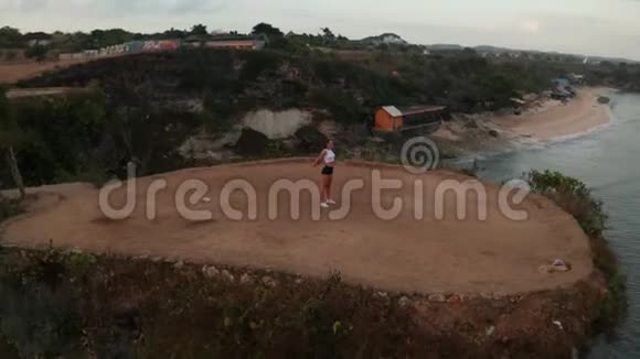 日出时在海边悬崖上运动的女性的鸟瞰图视频的预览图