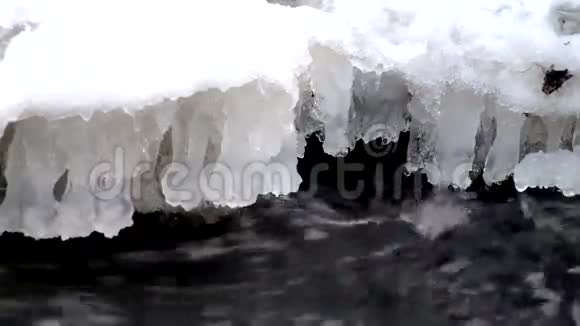 在山河清澈的冷水中冻住了雪白的大巨石小冰柱闪烁在嘈杂的溪流的水晶水之上视频的预览图
