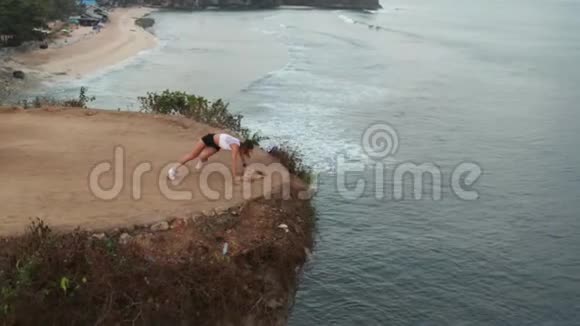 日出时在海边悬崖上运动后女性休息的鸟瞰图视频的预览图