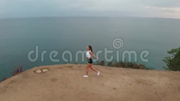 日出时在海边悬崖上运动的女性的鸟瞰图视频的预览图