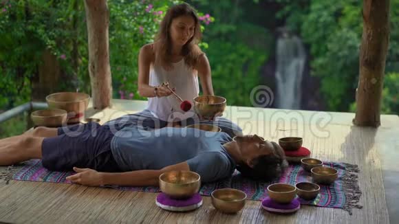 一位亚洲圣药大师为一位年轻的客户表演藏碗治疗仪式的女子拍摄的超慢镜头视频的预览图