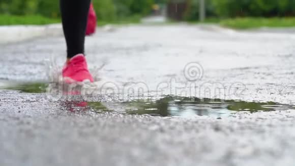 穿运动鞋的跑步者的腿运动女人在户外慢跑踩在泥泞的水坑里单跑运动员在雨中奔跑视频的预览图