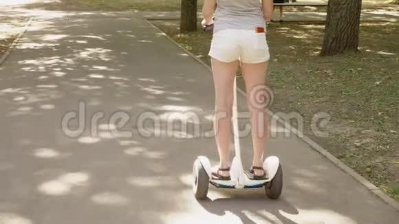 穿白色短裤的女孩在晴朗的晴天骑着赛格威夏天公园和阳光4k慢镜头拍摄视频的预览图