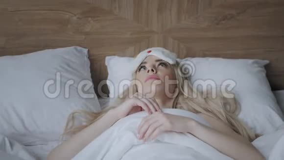 年轻女子睡在舒适的床上戴着面具睡觉眼睛上的眼罩早上在酒店房间白色枕头和视频的预览图