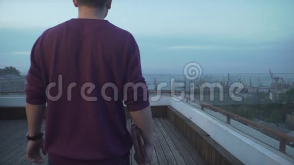 乌云密布的天黑头发的男人手里拿着日记穿着便服看着海港海景在木顶上散步视频的预览图