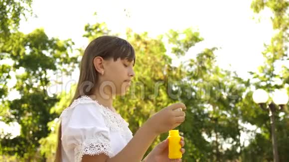 美丽的女孩在春天夏天和微笑的公园里吹肥皂泡慢动作年轻女孩在玩视频的预览图