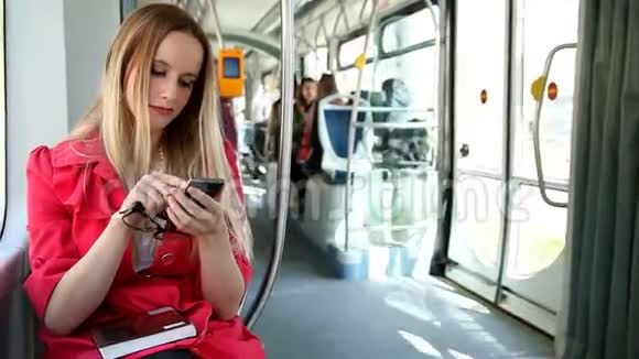 漂亮的金发女人坐着电车在手机上打字打电话打手机拿着眼镜视频的预览图
