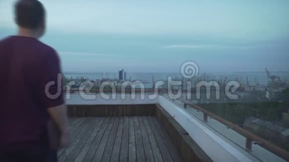 乌云密布的天黑头发的男人手里拿着日记穿着便服看着海边的港口走在木顶上视频的预览图