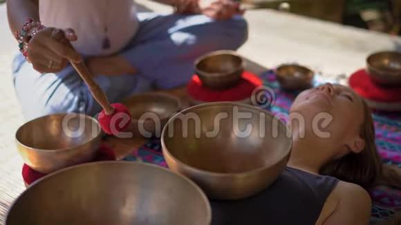 一位亚洲圣药大师为一位年轻的客户表演藏碗治疗仪式的女子拍摄的超慢镜头视频的预览图