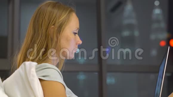 一位年轻女士用笔记本电脑工作她坐在床上背着一个背景的摩天轮的轮廓视频的预览图