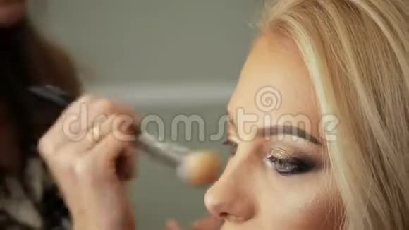 美容美发化妆师用一个金发碧眼的女人画眼睛上的阴影视频的预览图