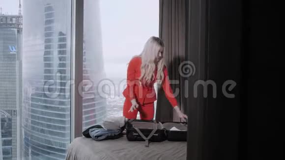 年轻的金发女商人来到一个带黑色手提箱的酒店房间穿红珊瑚商务套装的女人少女视频的预览图