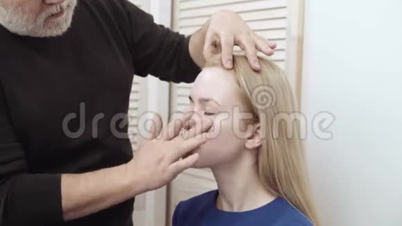 化妆师给一个有魅力的年轻女人化妆为年轻女孩化妆美容院的年轻女孩金发碧眼视频的预览图