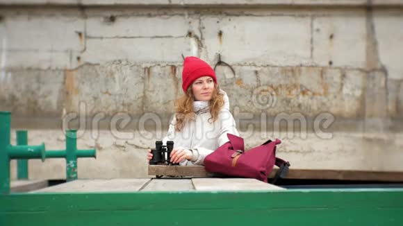 一个穿着夹克和红帽子的美女站在码头上用望远镜看着视频的预览图