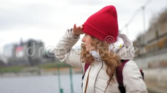 一个穿着夹克和红帽子的美女站在码头上用望远镜看着视频的预览图