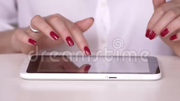那个女人在平板电脑上工作做红色指甲的女商人穿白衬衫的女人看着有关视频的预览图