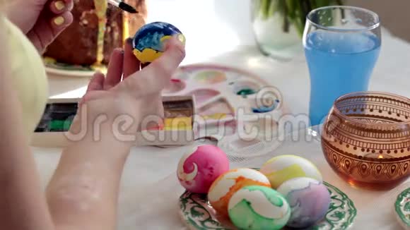 红发女孩用刷子涂复活节彩蛋在桌子上复活节蛋糕鸡蛋糖果花束视频的预览图