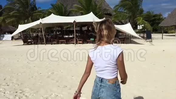 一个迷人的女孩沿着海滩散步用相机调情慢动作视频的预览图