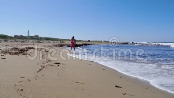 年轻的女人穿着红色的裙子在沙滩上奔跑享受阳光摆姿势泼水和风吹慢动作视频的预览图