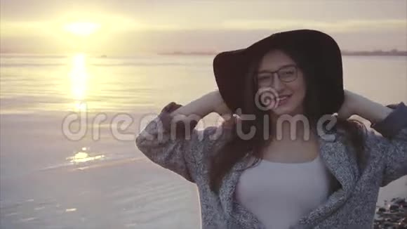 日落时分海边戴着黑色帽子和眼镜的年轻美女视频的预览图