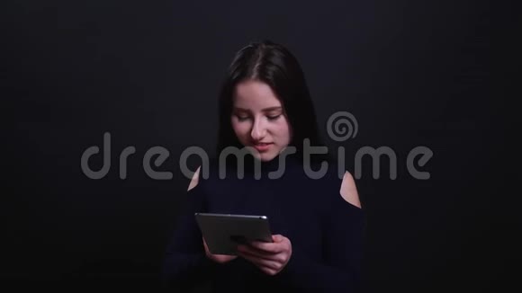 年轻漂亮的黑发女性的特写肖像使用平板电脑背景与黑色隔离视频的预览图