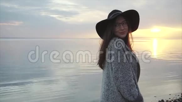 日落时分海边戴着黑色帽子和眼镜的年轻美女视频的预览图