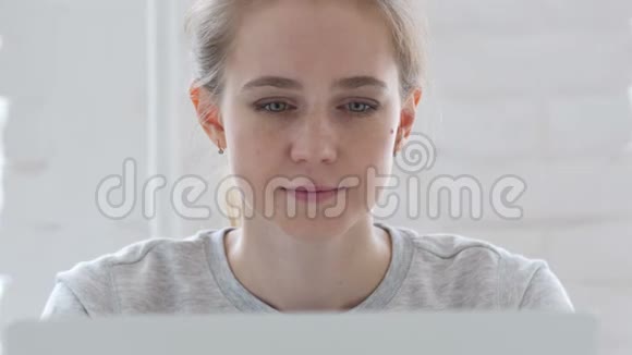 在笔记本电脑上工作时看镜头的年轻女子视频的预览图