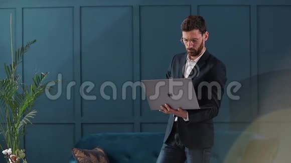 一位优雅的商人的肖像在豪华的蓝色办公室内部有笔记本电脑视频的预览图