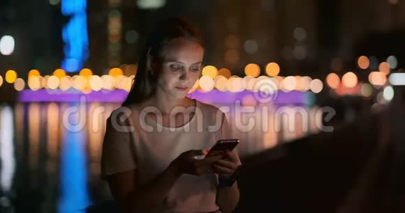 夜城背景下的一个年轻女孩看着智能手机屏幕视频的预览图