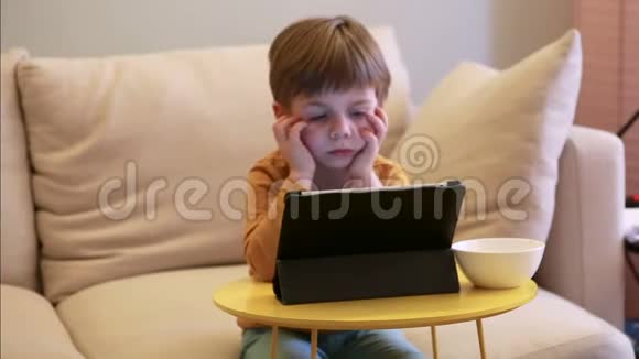 孩子在家里的床上使用平板电脑沙发上可爱的男孩正在看卡通玩游戏从笔记本电脑上学习教育娱乐视频的预览图