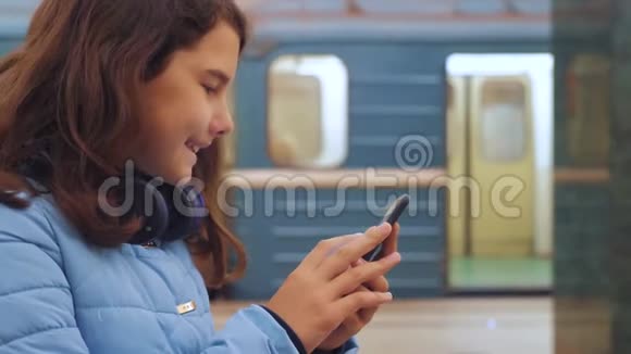 十几岁的女孩带着智能手机和耳机等待地铁很多人聚集在地下地铁地下工程视频的预览图