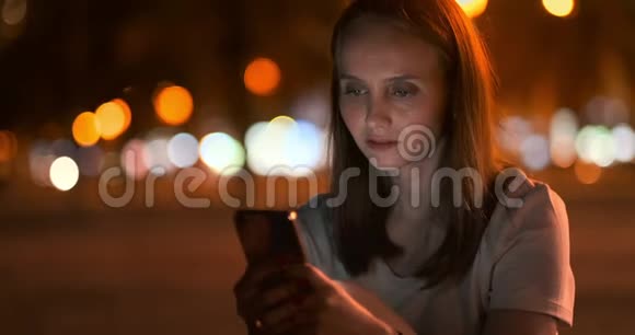 夜城的年轻女孩在智能手机上写短信视频的预览图