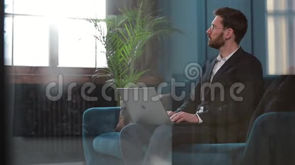 一位优雅的商人坐在豪华蓝色办公室内部的沙发上手提电脑的肖像视频的预览图