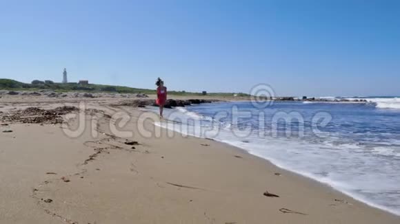 年轻的女人穿着红色的裙子在沙滩上奔跑享受阳光摆姿势泼水和风吹视频的预览图