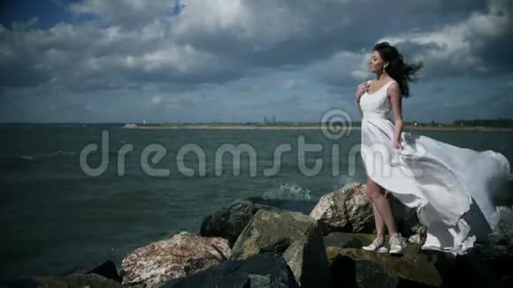 穿着白色连衣裙的漂亮女孩站在海滨视频的预览图