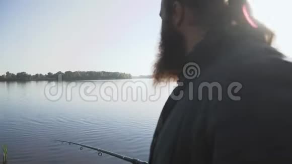 长胡子的人在河岸上钓鱼渔夫拿着鱼竿在河上钓鱼河流捕鱼视频的预览图
