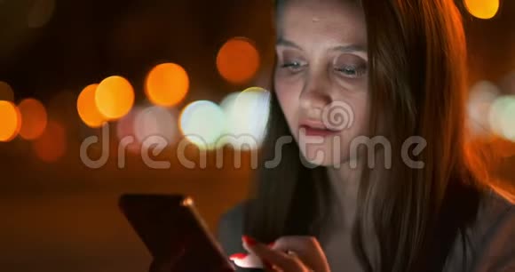 夜城的年轻女孩在智能手机上写短信视频的预览图