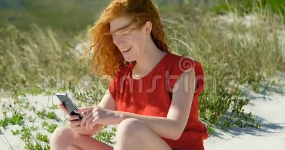 阳光明媚的一天女人在海滩上用手机视频的预览图