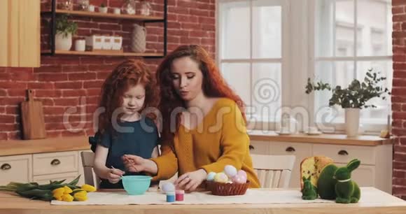 妈妈和她的小女儿正在准备复活节幸福的家庭在舒适的厨房里准备画复活节彩蛋视频的预览图