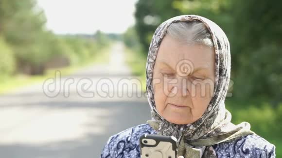 成熟的老太太在户外拿着银色智能手机视频的预览图