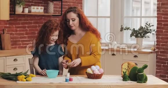 妈妈和她的小女儿正在准备复活节幸福的家庭在舒适的厨房里准备画复活节彩蛋视频的预览图