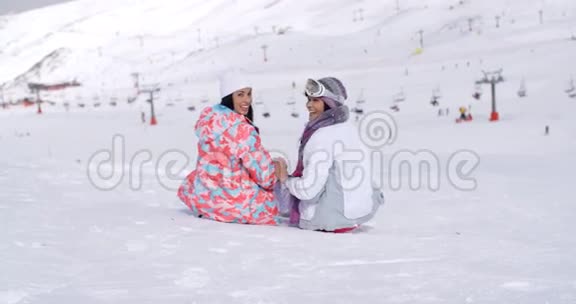 两个年轻女子坐在滑雪场的雪地里视频的预览图