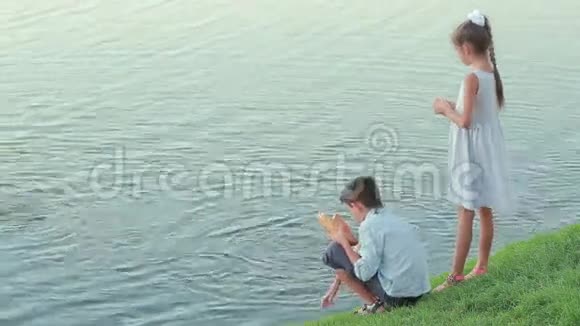 穿着粉红色衣服在花园池塘里喂鱼的小女孩湖边的孩子视频的预览图