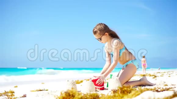 可爱的小女孩在海滩度假时玩玩具和制作沙堡视频的预览图