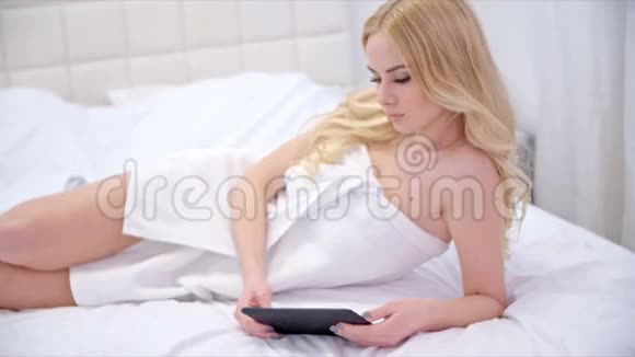 美丽的金发女孩躺在床上和桌子视频的预览图