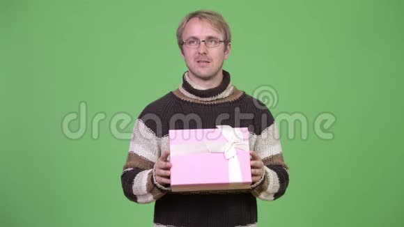 摄影棚拍摄的快乐帅哥一边思考一边拿着礼品盒视频的预览图