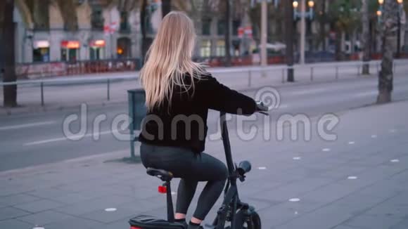 漂亮的金发女人在城市里驾驶电动自行车视频的预览图