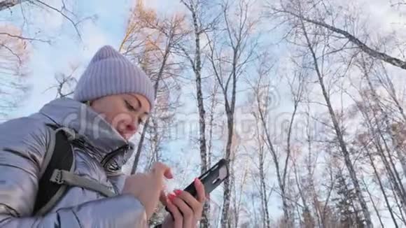女人在树林里散步旅行者在森林的电话里被拍照女孩做自拍和沟通视频的预览图